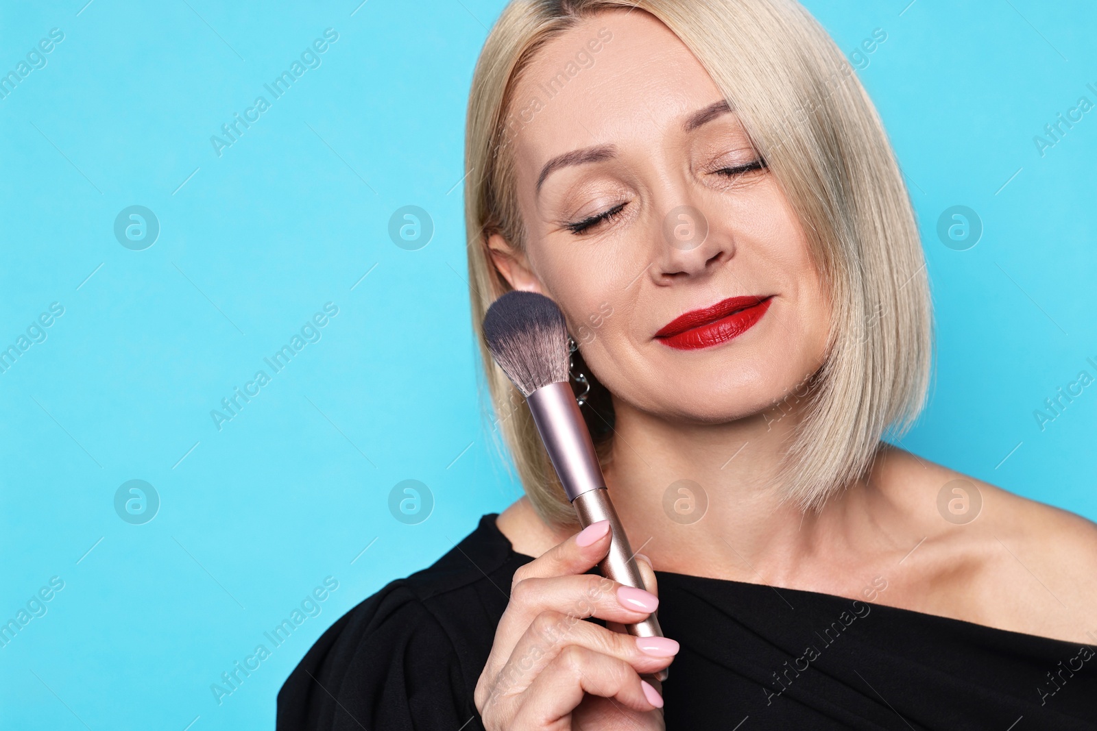 Photo of Woman with makeup brush on light blue background. Space for text