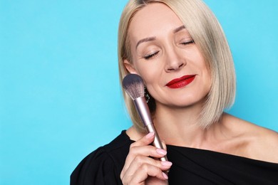 Photo of Woman with makeup brush on light blue background. Space for text