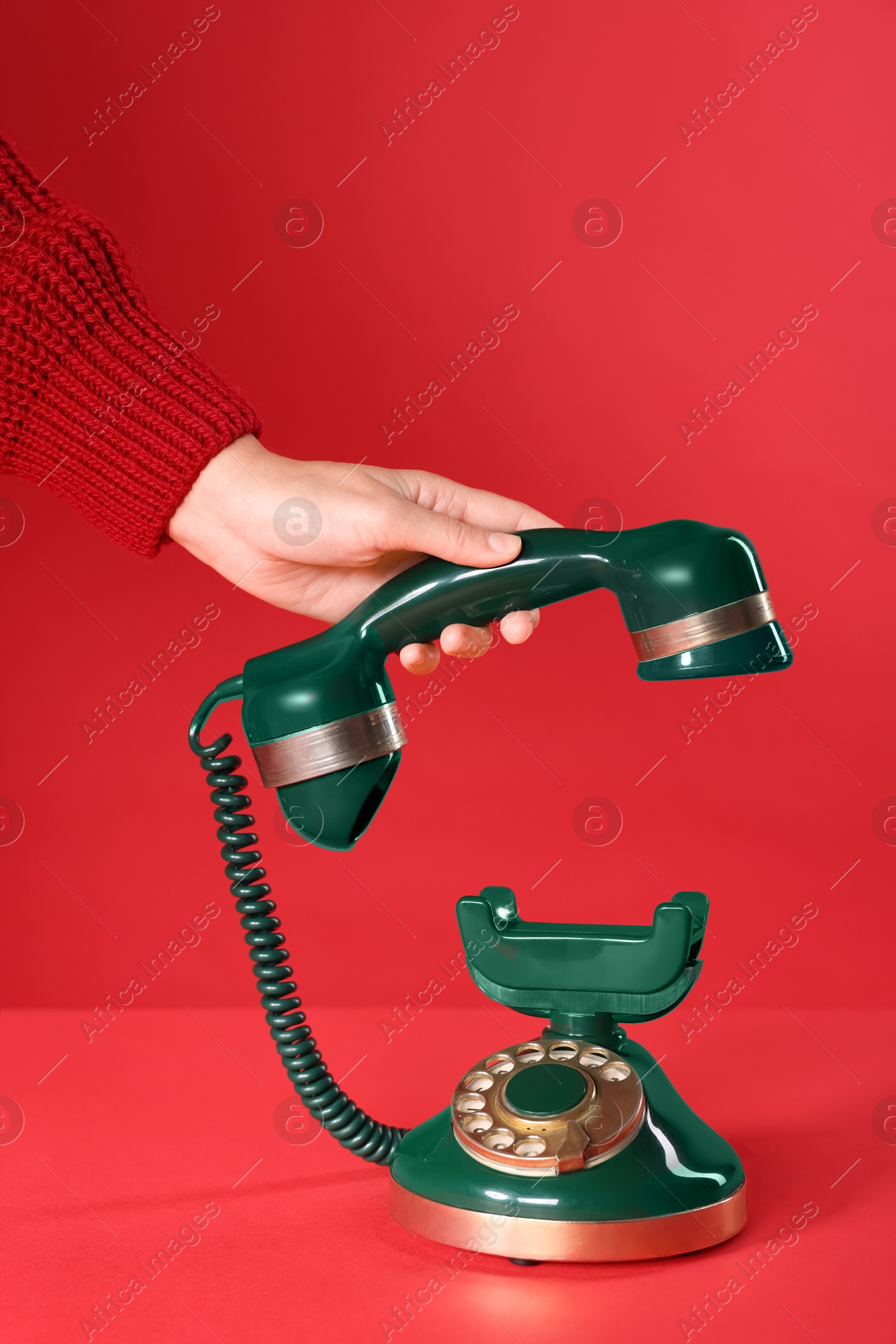 Photo of Woman holding receiver of green vintage telephone on red background, closeup