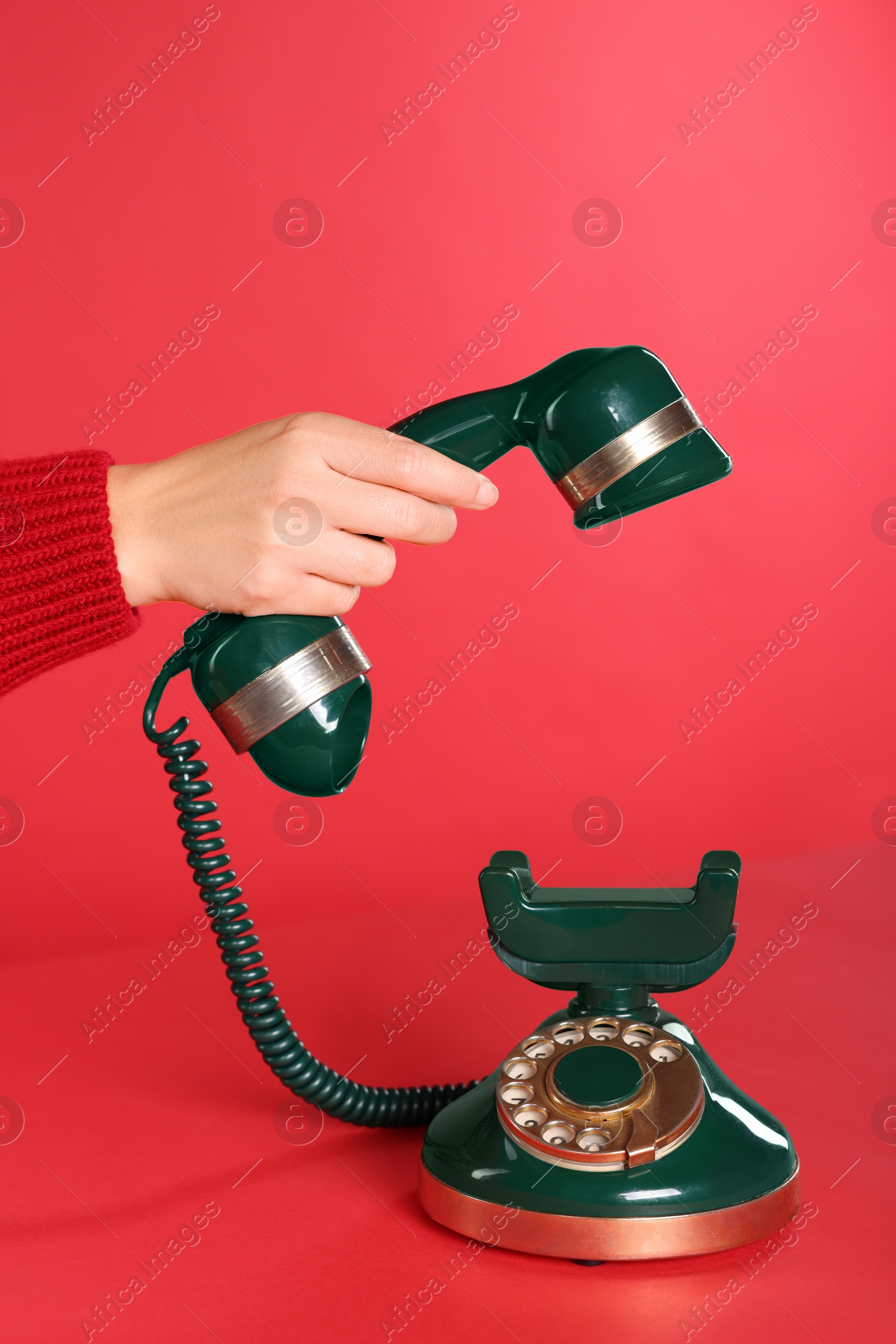 Photo of Woman holding receiver of green vintage telephone on red background, closeup