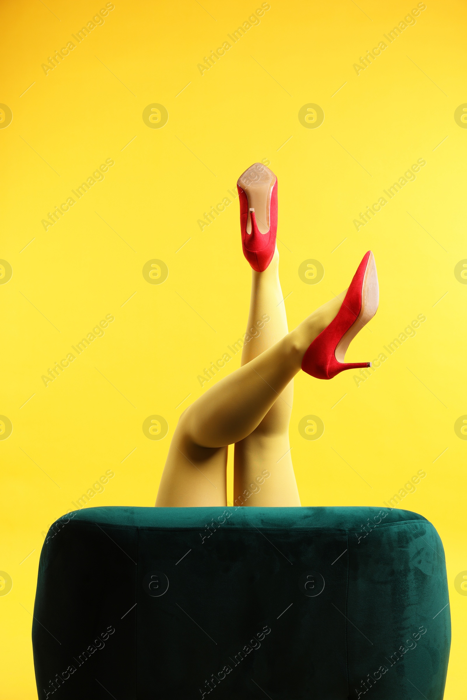 Photo of Woman in red shoes showing legs on yellow background, closeup