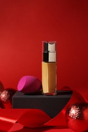 Christmas present. Liquid foundation, sponge, gift box and festive decor on red background