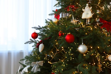 Christmas tree decorated with beautiful ornaments and lights indoors, closeup