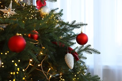 Christmas tree decorated with beautiful ornaments and lights indoors, closeup