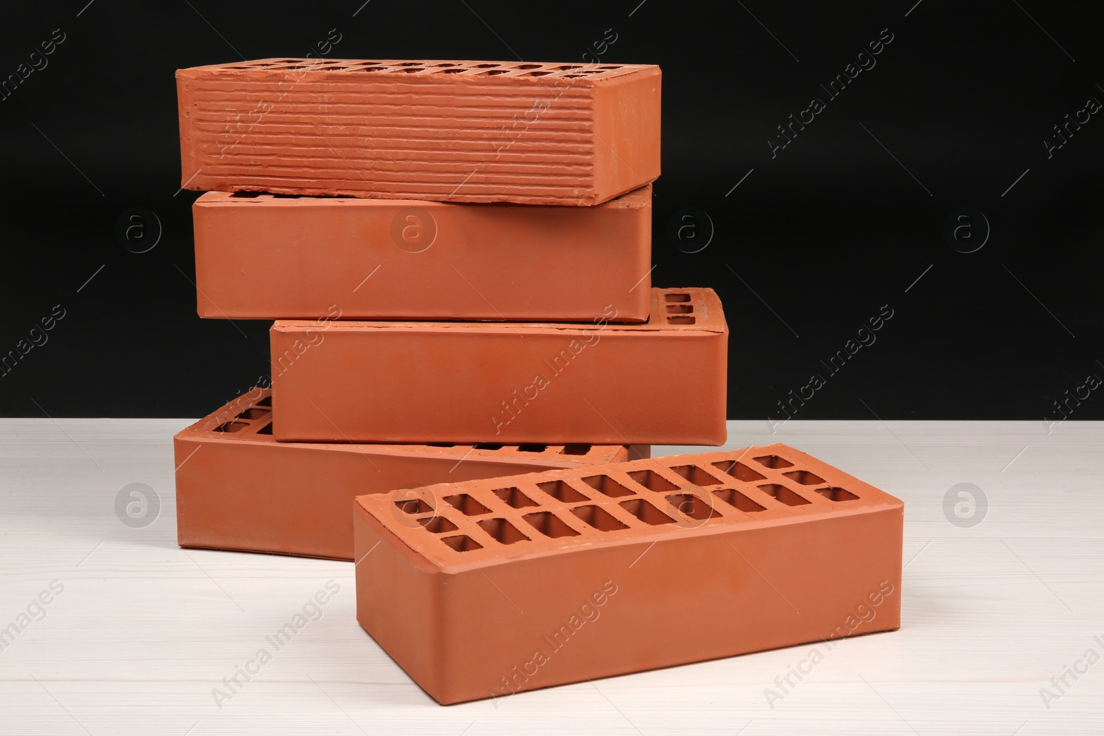 Photo of Many red bricks on light wooden table against black background. Building material