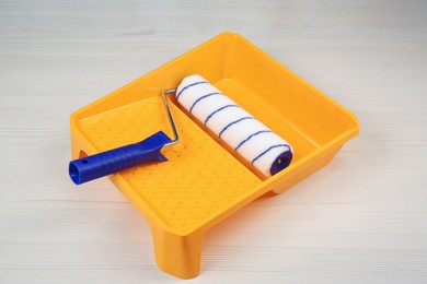 Photo of Paint roller and tray on light wooden table against black background