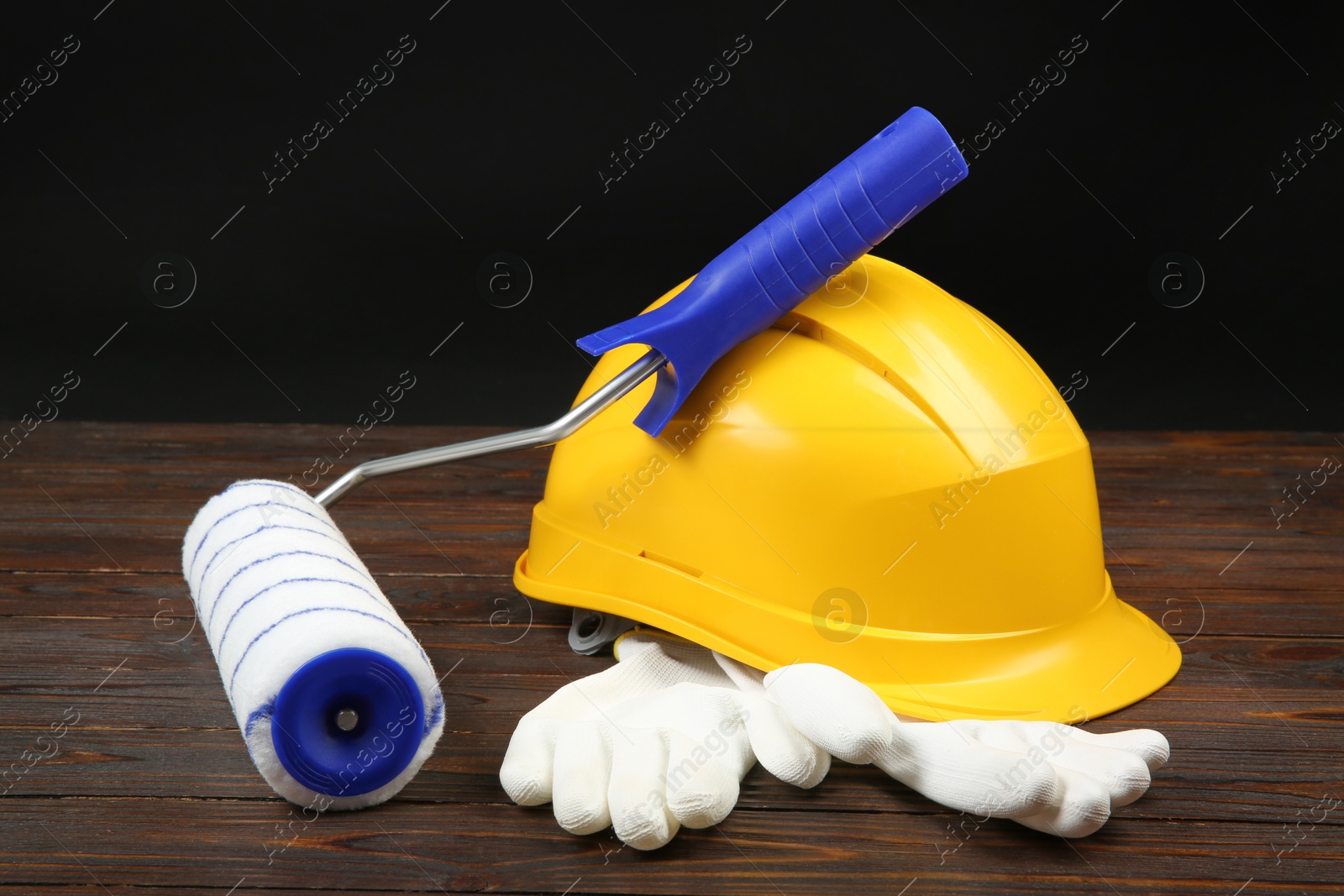 Photo of Yellow hard hat, paint roller and rubber gloves on wooden table