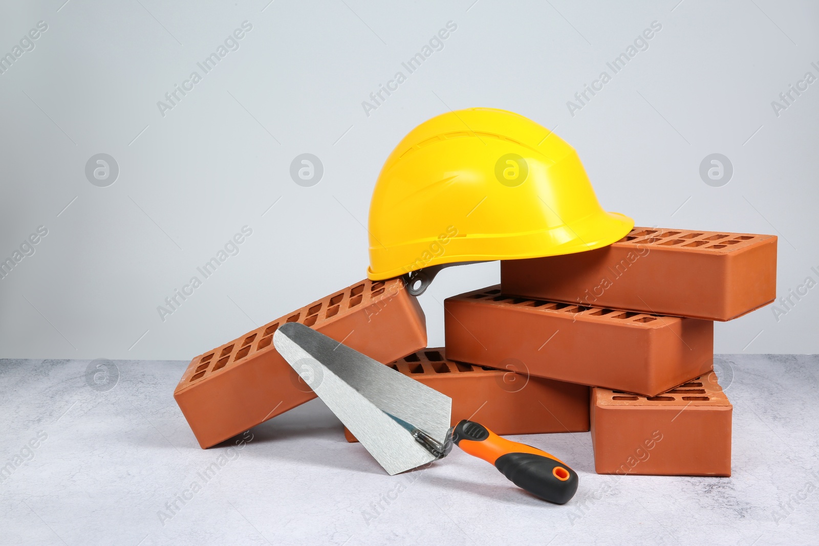 Photo of Red bricks, trowel and hardhat on textured table against light background