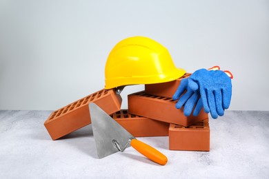 Photo of Red bricks, trowel, gloves and hardhat on textured table against light background