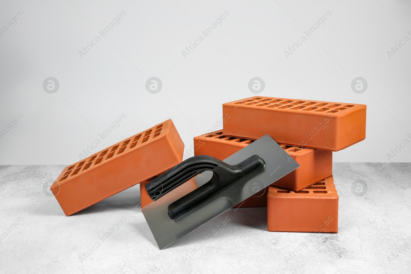 Photo of Red bricks and plastering trowel on textured table against light background. Building material