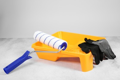 Photo of Paint roller, gloves and yellow tray on textured table against light background. Building material