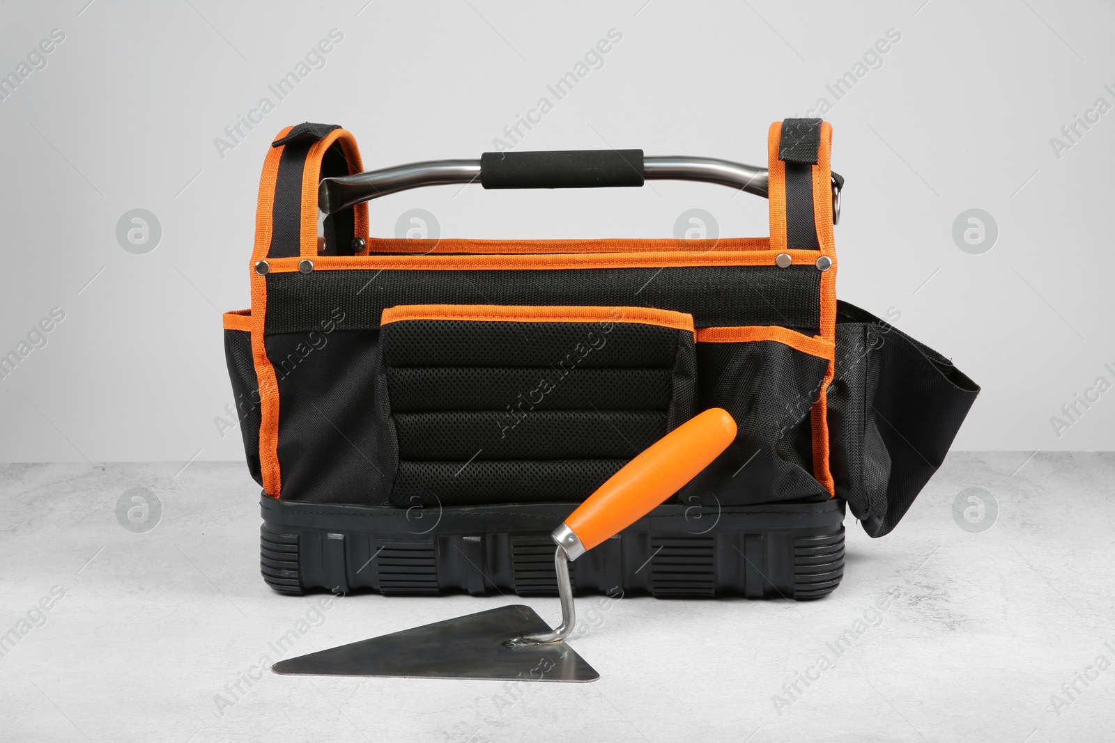 Photo of Bag for construction tools and trowel on textured table against light background