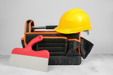 Photo of Bag for construction tools, hard hat and trowel on textured table against light background