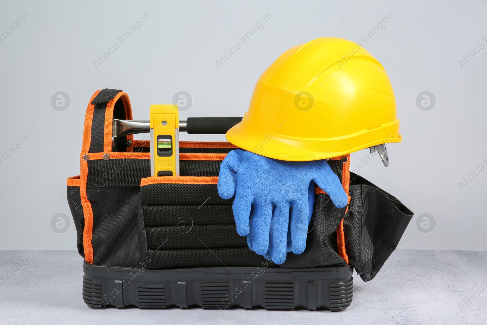 Photo of Bag for construction tools, building level, hard hat and glove on textured table against light background