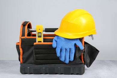 Photo of Bag for construction tools, building level, hard hat and glove on textured table against light background