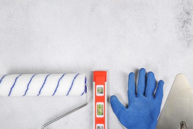 Photo of Paint roller, glove, building level and trowel on light textured table, flat lay. Space for text