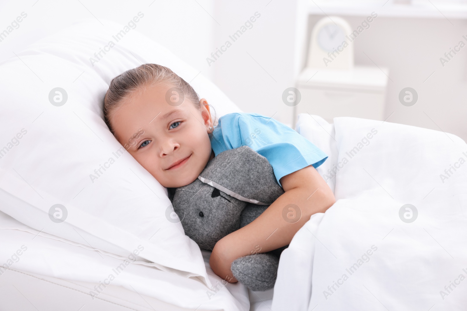 Photo of Cute little girl with toy bunny on bed in hospital