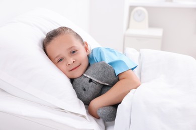 Cute little girl with toy bunny on bed in hospital