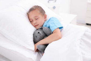 Cute little girl with toy bunny on bed in hospital