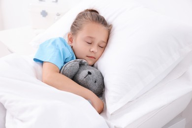 Cute little girl with toy bunny on bed in hospital