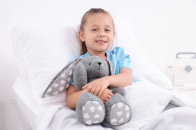 Cute little girl with toy bunny on bed in hospital