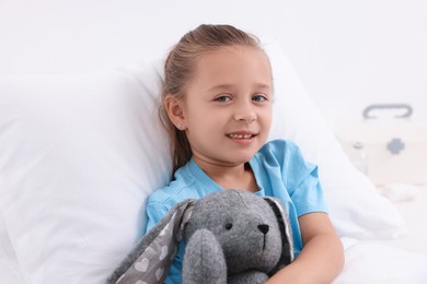 Photo of Cute little girl with toy bunny on bed in hospital