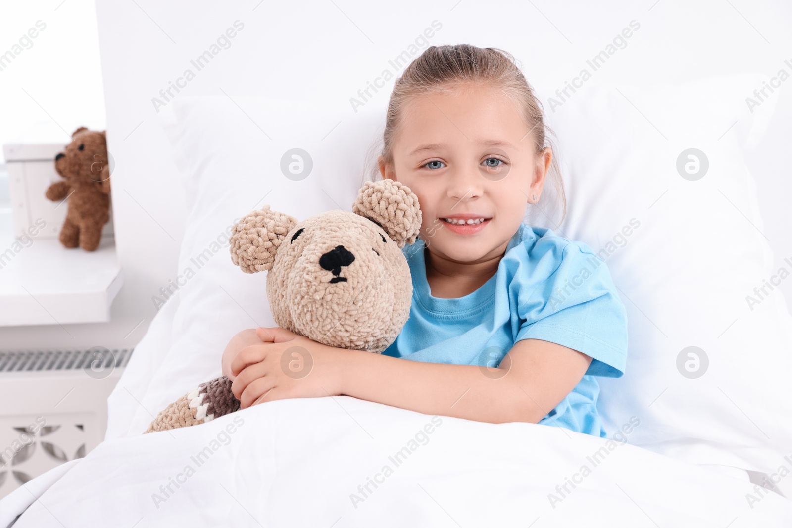 Photo of Cute little girl with teddy bear on bed in hospital