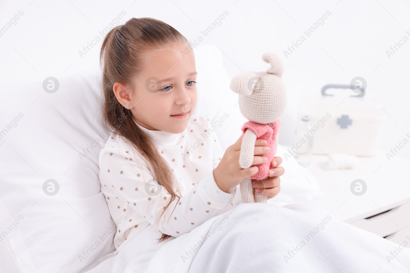 Photo of Cute little girl with toy bunny on bed in hospital