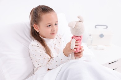 Cute little girl with toy bunny on bed in hospital