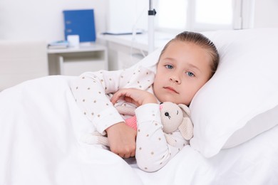 Cute little girl with toy bunny on bed in hospital