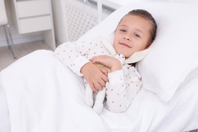 Cute little girl with toy bunny on bed in hospital