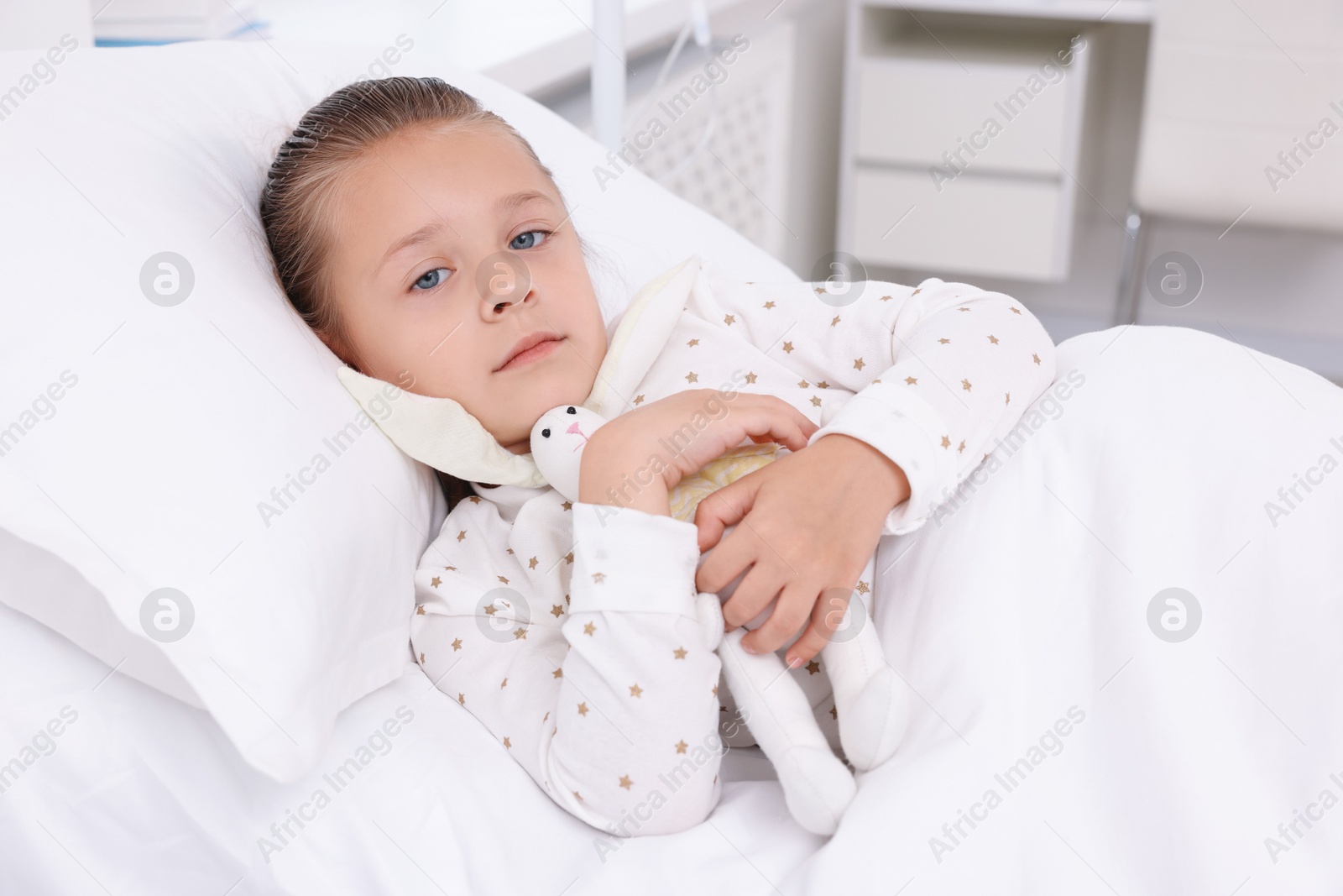 Photo of Cute little girl with toy bunny on bed in hospital