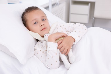 Cute little girl with toy bunny on bed in hospital