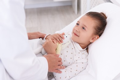 Photo of Doctor examining little girl on bed at hospital, closeup