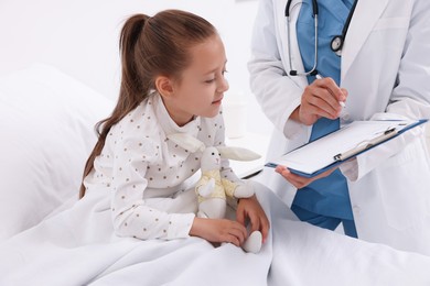 Photo of Doctor examining little girl on bed at hospital, closeup