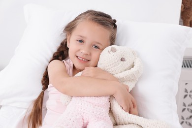 Photo of Cute little girl with toy bunny on bed in hospital