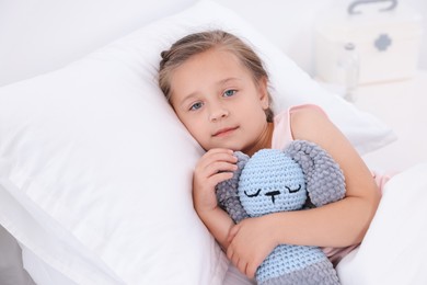 Cute little girl with toy bunny on bed in hospital