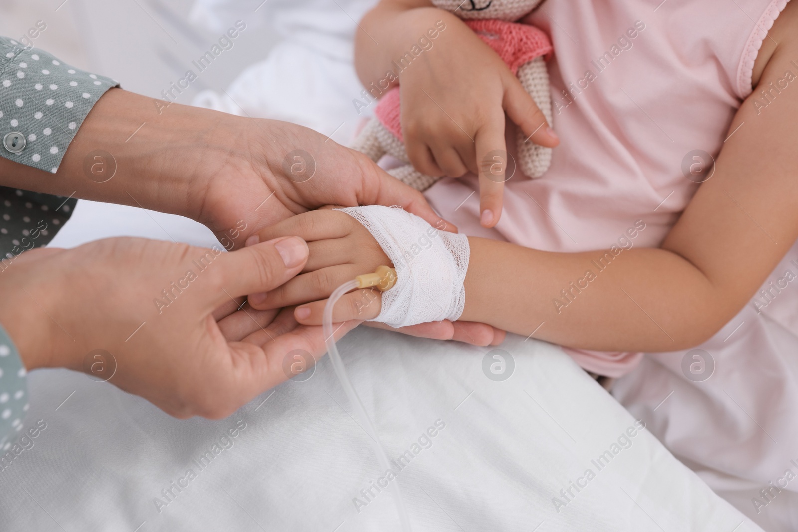 Photo of Mother and her little daughter with IV drip on bed in hospital, closeup