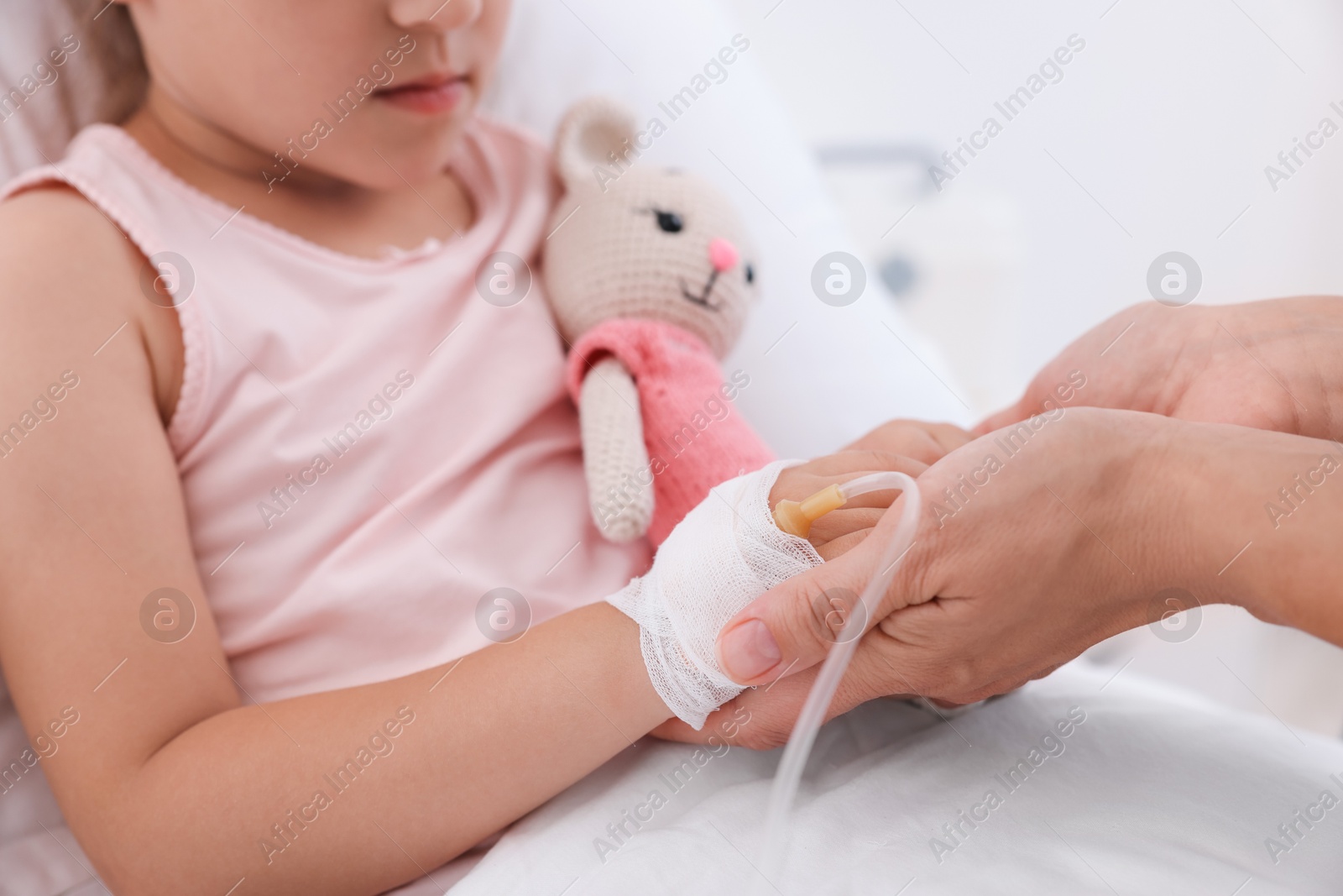 Photo of Mother and her little daughter with IV drip on bed in hospital, closeup