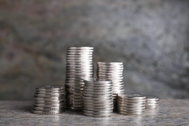 Photo of Stacked coins on wooden table against blurred grey background, closeup. Salary concept