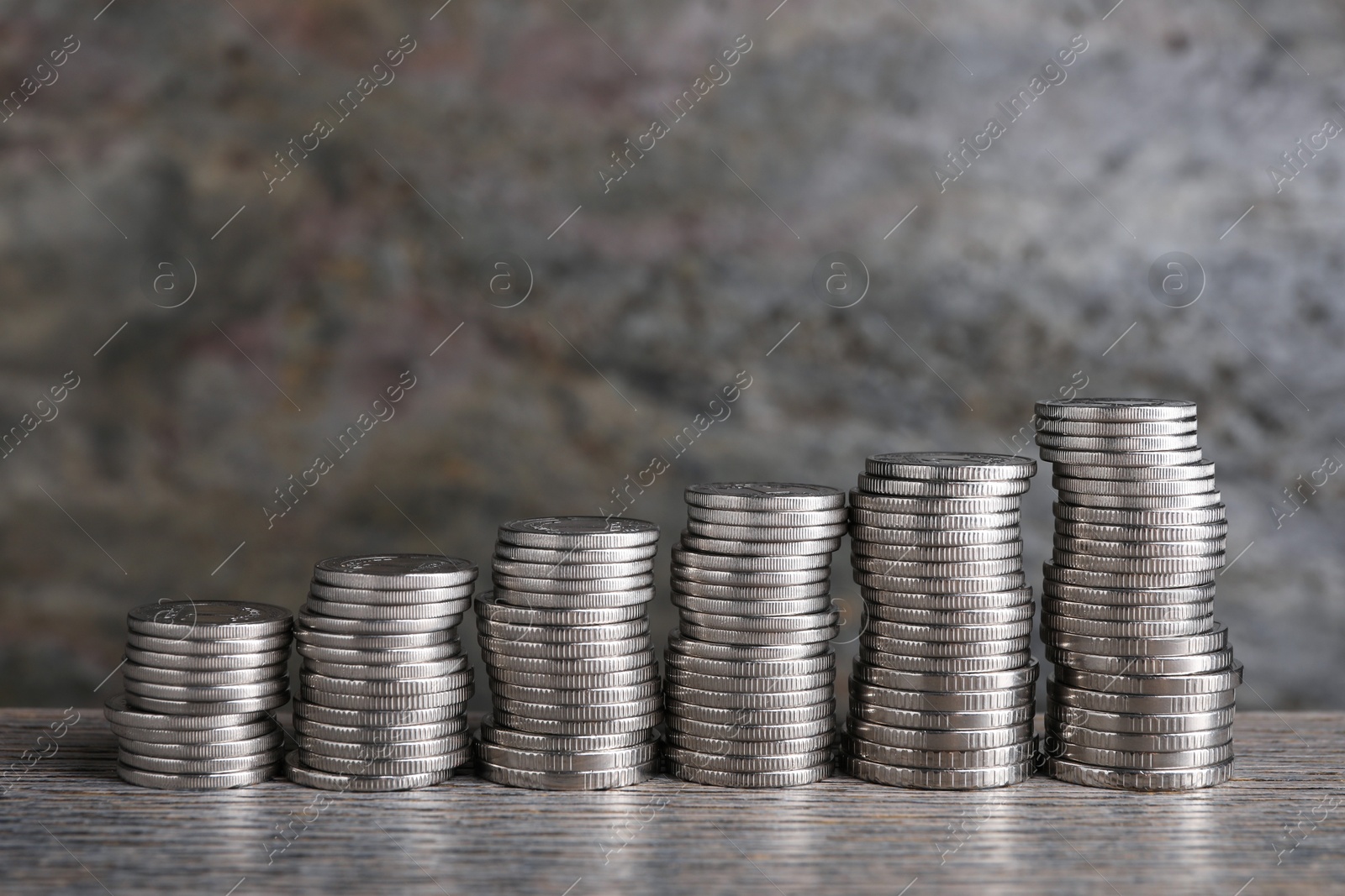 Photo of Stacked coins on wooden table against blurred grey background, closeup. Salary concept