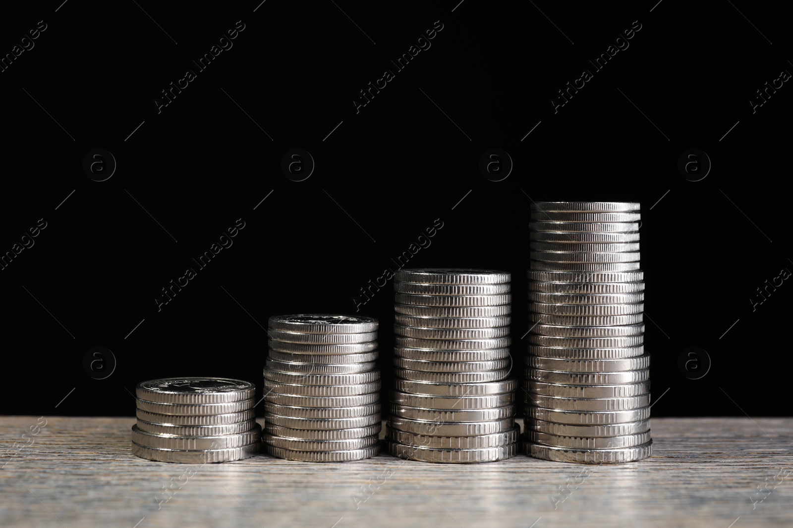 Photo of Stacked coins on wooden table against black background, closeup. Salary concept