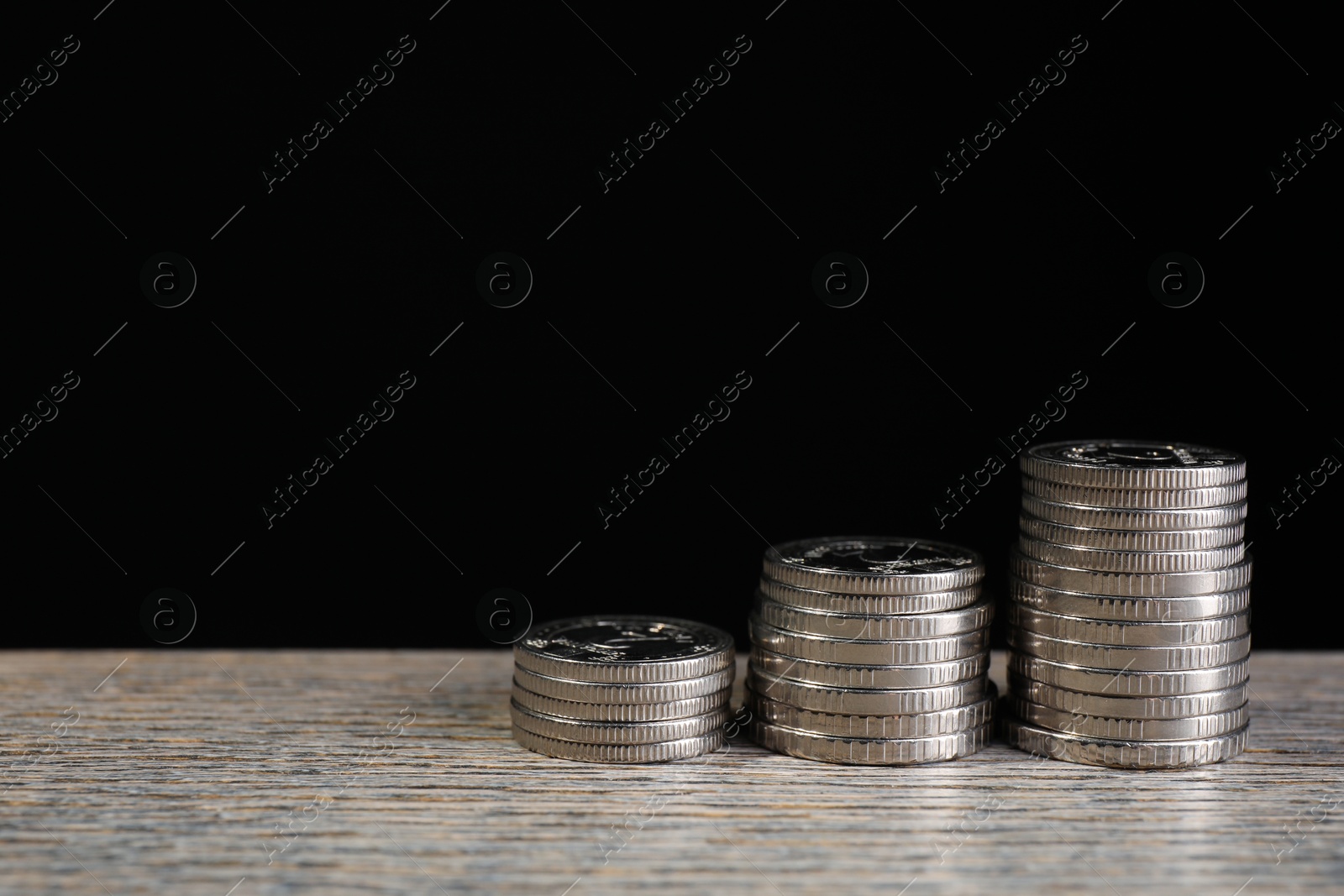 Photo of Stacked coins on wooden table against black background, closeup with space for text. Salary concept