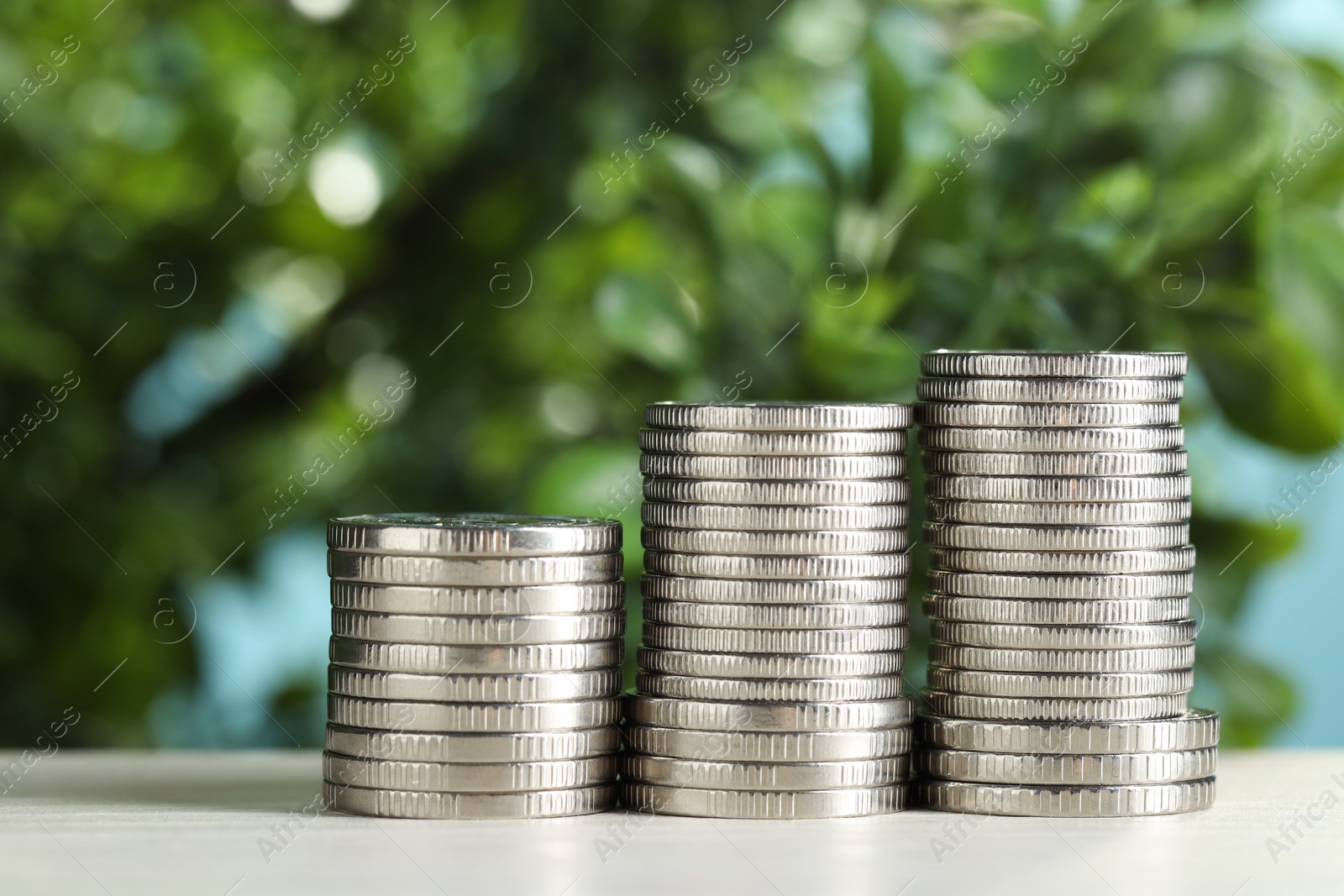 Photo of Stacked coins on white table against blurred green background, closeup. Salary concept