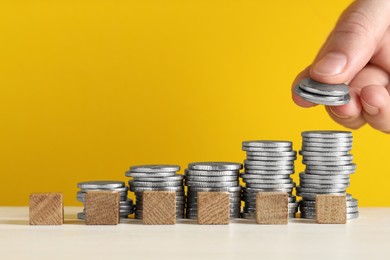 Photo of Woman putting coins and cubes with word Salary at white table against yellow background, closeup. Space for text