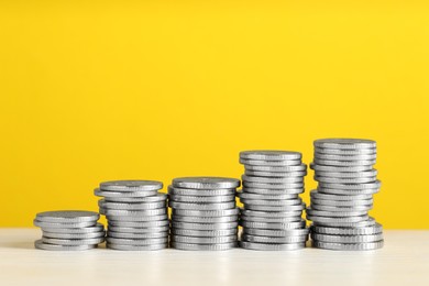 Photo of Stacked coins on white wooden table against yellow background, closeup with space for text. Salary concept