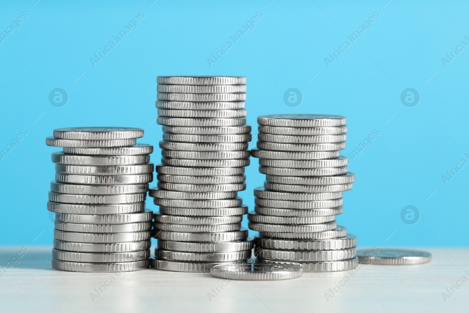 Photo of Stacked coins on white wooden table against light blue background, closeup. Salary concept