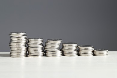 Photo of Stacked coins on white wooden table against grey background. Salary concept