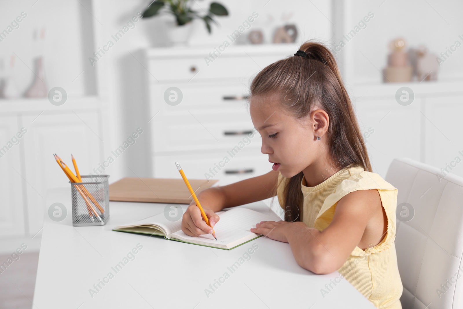 Photo of Girl with correct posture doing homework at white desk indoors