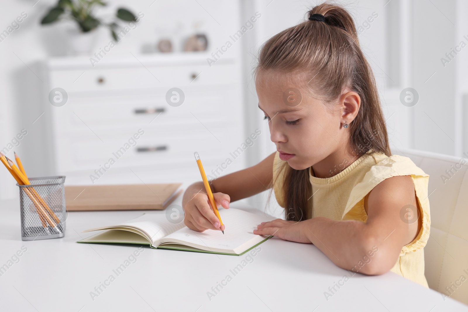 Photo of Girl with correct posture doing homework at white desk indoors